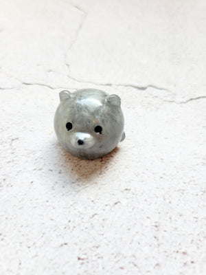 A small round bear figure with black painted eyes and nose. It's silver in color.