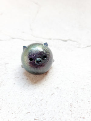 A small round pig figure with black painted eyes and nose. It's colorshifting purples and greens.