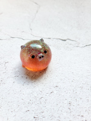 A small round pig figure with black painted eyes and nose. It's a yellow/orange color with fine glitter throughout.