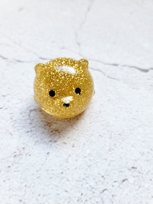 A small round bear figure with black painted eyes and nose. It's a gold glitter design.