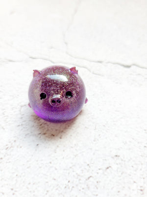 A small round pig figure with black painted eyes and nose. It's a deep purple color with fine gold glitter throughout.