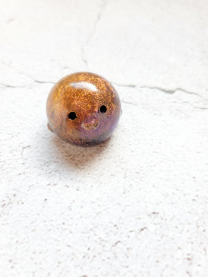 A small round penguin figure with painted black eyes. It's orange with hints of purple.