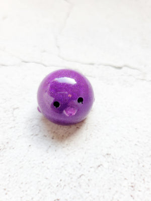 A small round duck figure, with black painted eyes. it's purple with fine glitter mixed in.
