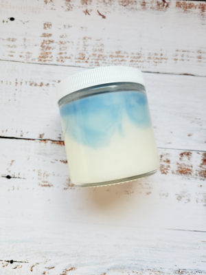 A side view of a 12oz marbled candle to show the light blue swirls in the wax. It's in a glass jar with a white lid. This candle is called Star Wars: Hoth. It's scent profile is ozone, mint, cypress.