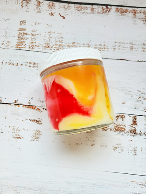 A 12oz marbled candle laying on its side to show the yellow and red swirls in the wax. It has a white lid and glass jar. This candle is called Wild Magic Surge: Fireball Necklace. It's scent profile is cinnamon, vanilla, smoke. It has a mystery Dungeons and Dragons die inside.