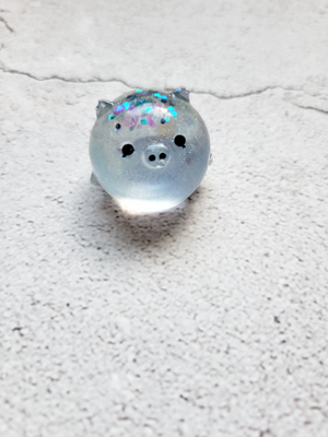 A small round pig figure with black painted eyes and nose. It's a transparent gray blue with glitter on the top of its head.