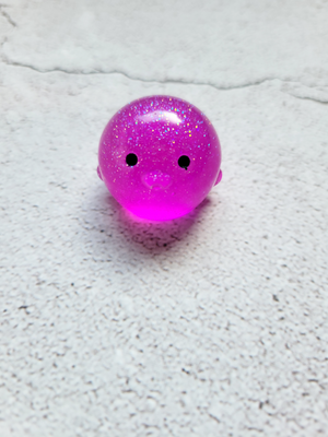 A small round penguin figure with black painted eyes. It's a bright pinkish purple with fine glitter within.