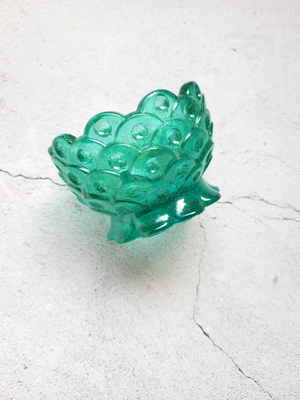 A side view of a tealight candle holder in the style of mermaid scales. It's transparent green.