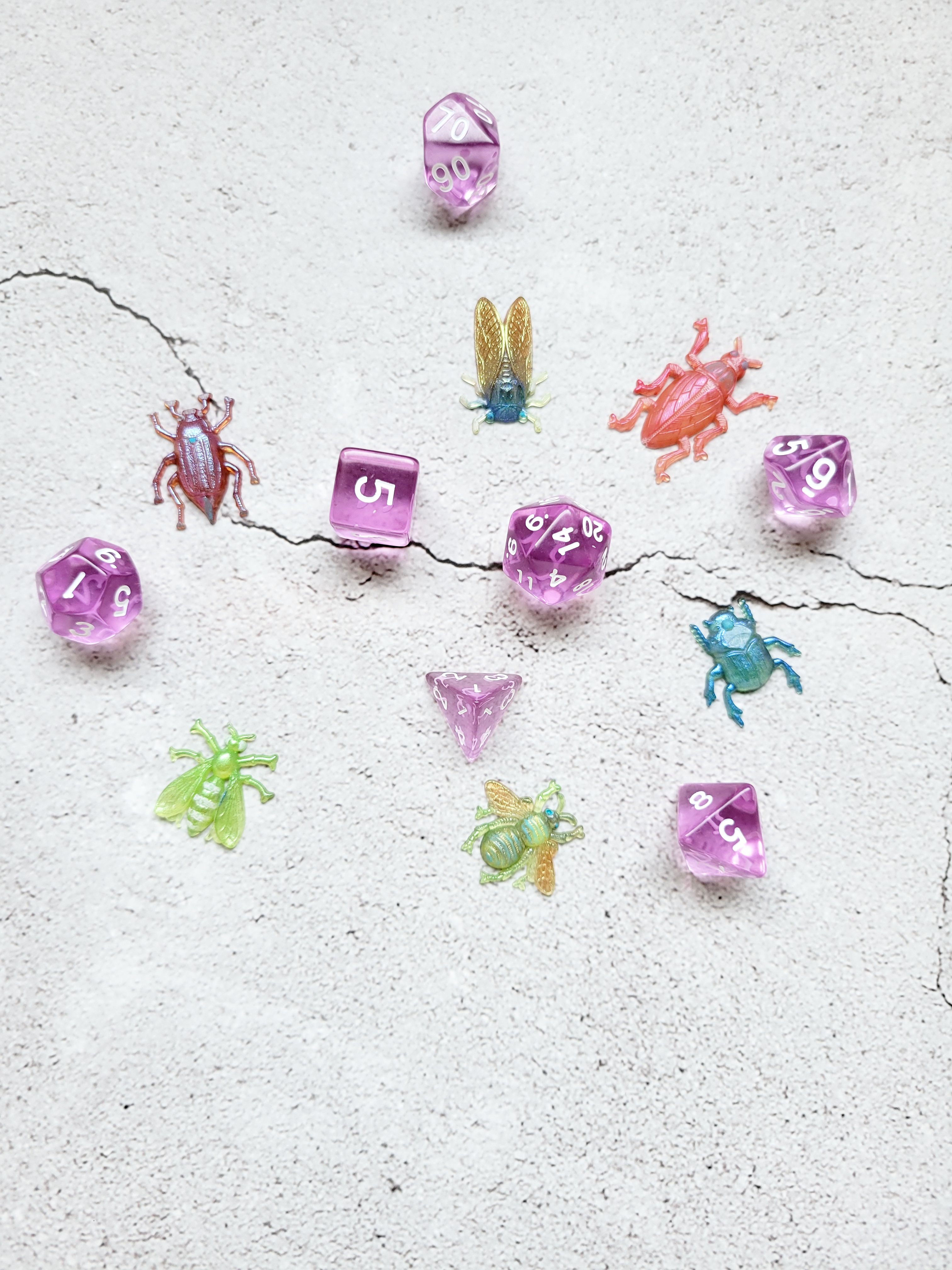 A birds eye view of a group of six various bugs. A peach beetle with pale blue painted eyes. A shimmering blue beetle. A lime green wasp. A green bee with blue eyes and yellow wings. A dark pink beetle with blue accents. A blue and gold cicada. They are encircled around a set of translucent purple standard D&D dice for scale.
