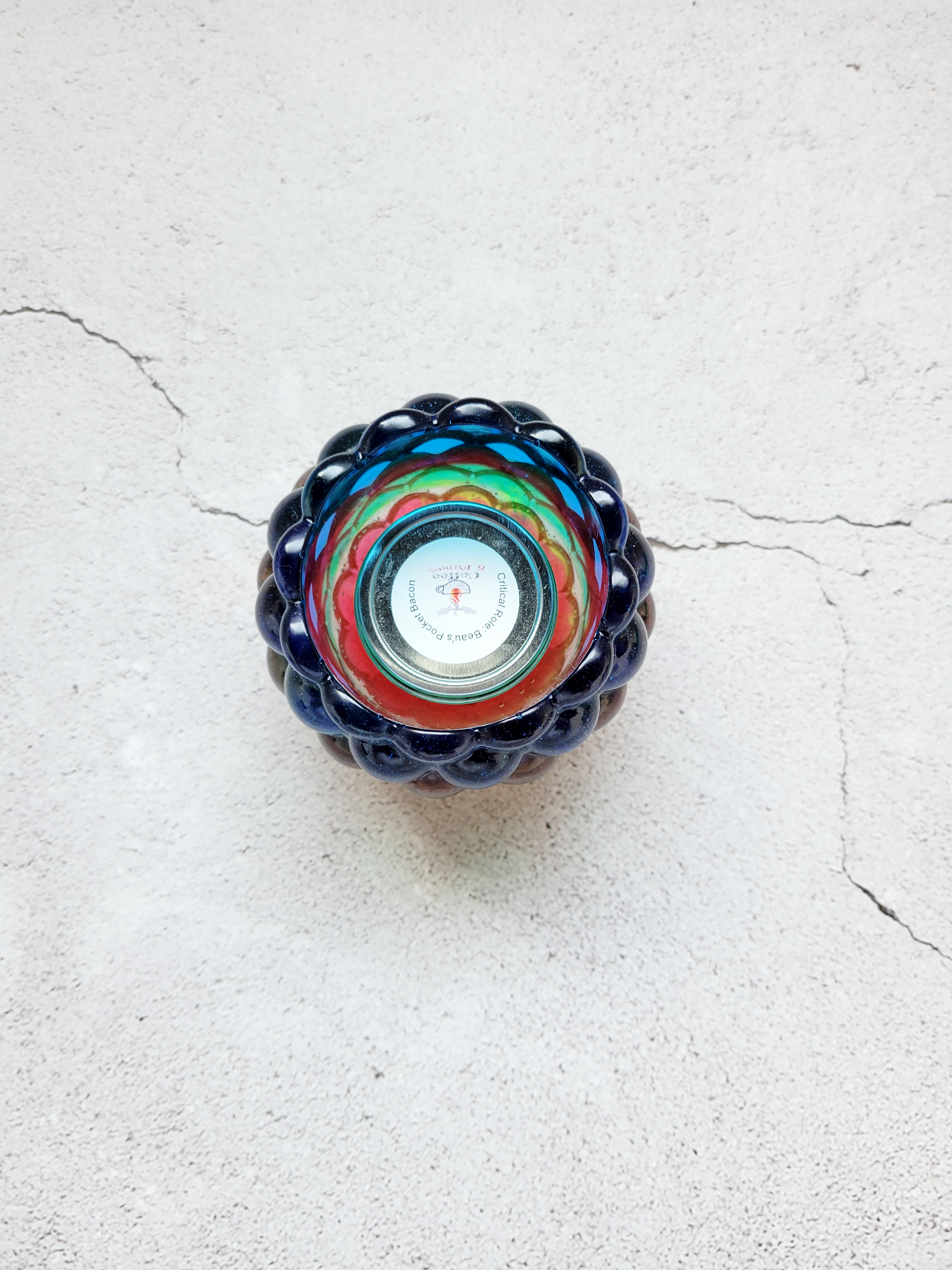 A top view of a tealight candle holder with a bubbled look. It's layered with colors of blue, red, green, orange. There is a tealight candle inside to show size comparison.