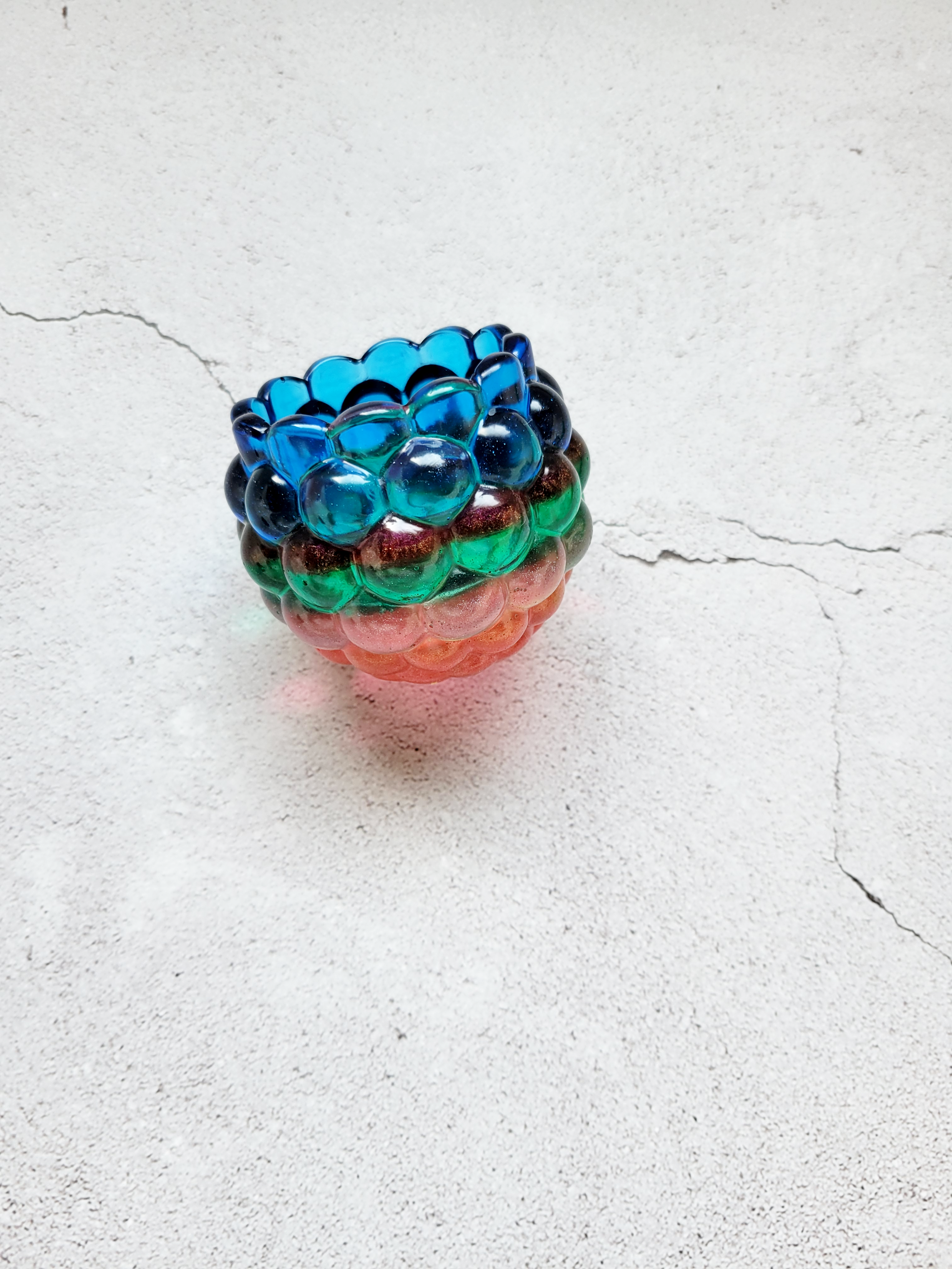 A side view of a tealight candle holder with a bubbled look. It's layered with colors of blue, red, green, orange.