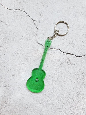 An acoustic guitar keychain with silver chain and ring hoop. It's transparent green.