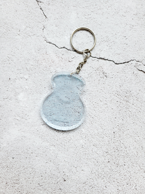 An acoustic guitar body keychain with a silver chain and ring hoop. It's a transparent blue.