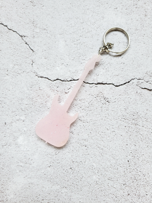 A pale pink electric guitar keychain with fine gold glitter mixed throughout. It's connected at the guitar head with silver chain and hoop.