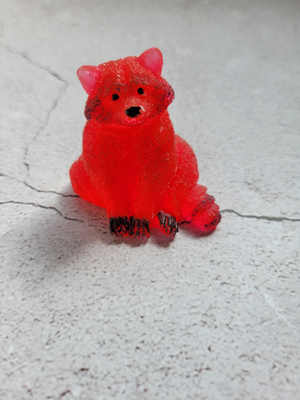 A front view of a sitting raccoon figure. He's a bright red with black painted eyes, nose, paws, and fur patches.