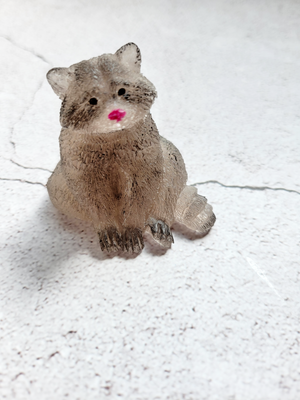 A front view of a sitting raccoon figure. He's got black painted eyes and red painted nose. He's a light gray color with black painted patches. 