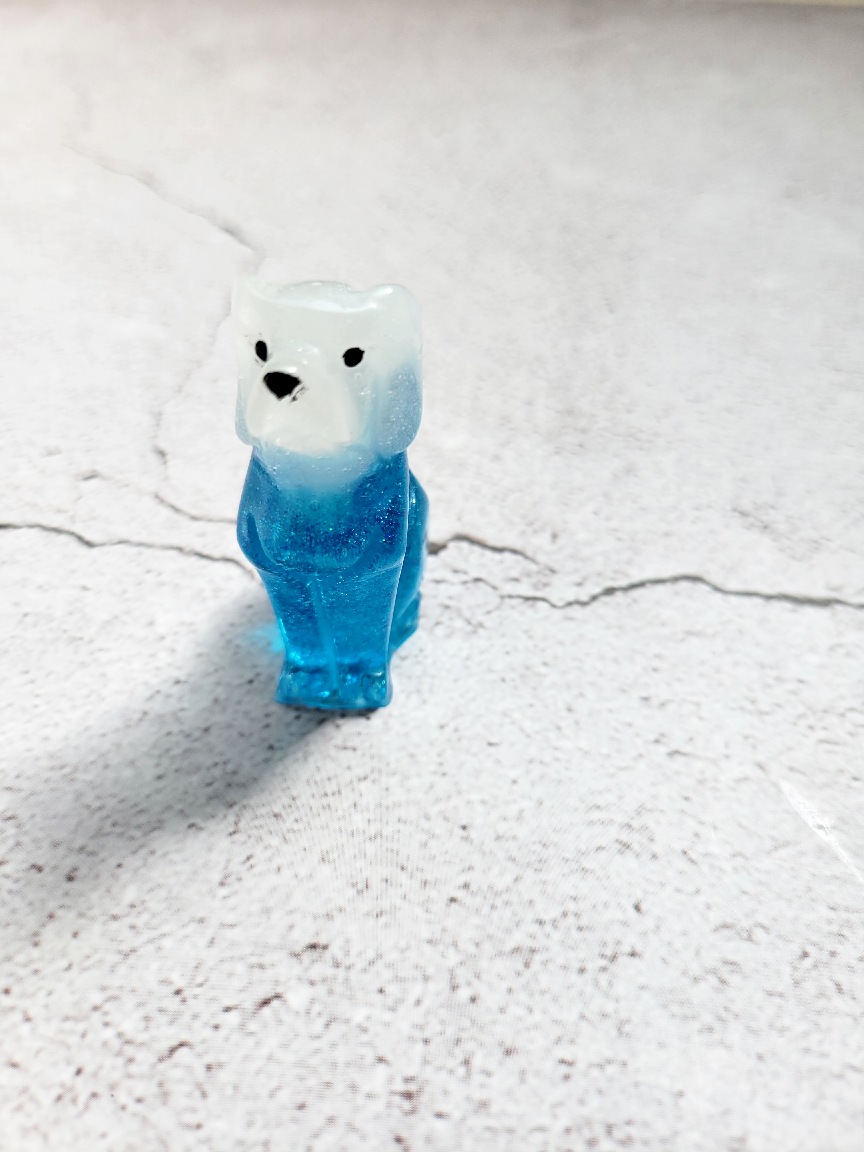 A front view of a tall slim dog figure with a translucent blue body, white head, black painted eyes and nose.