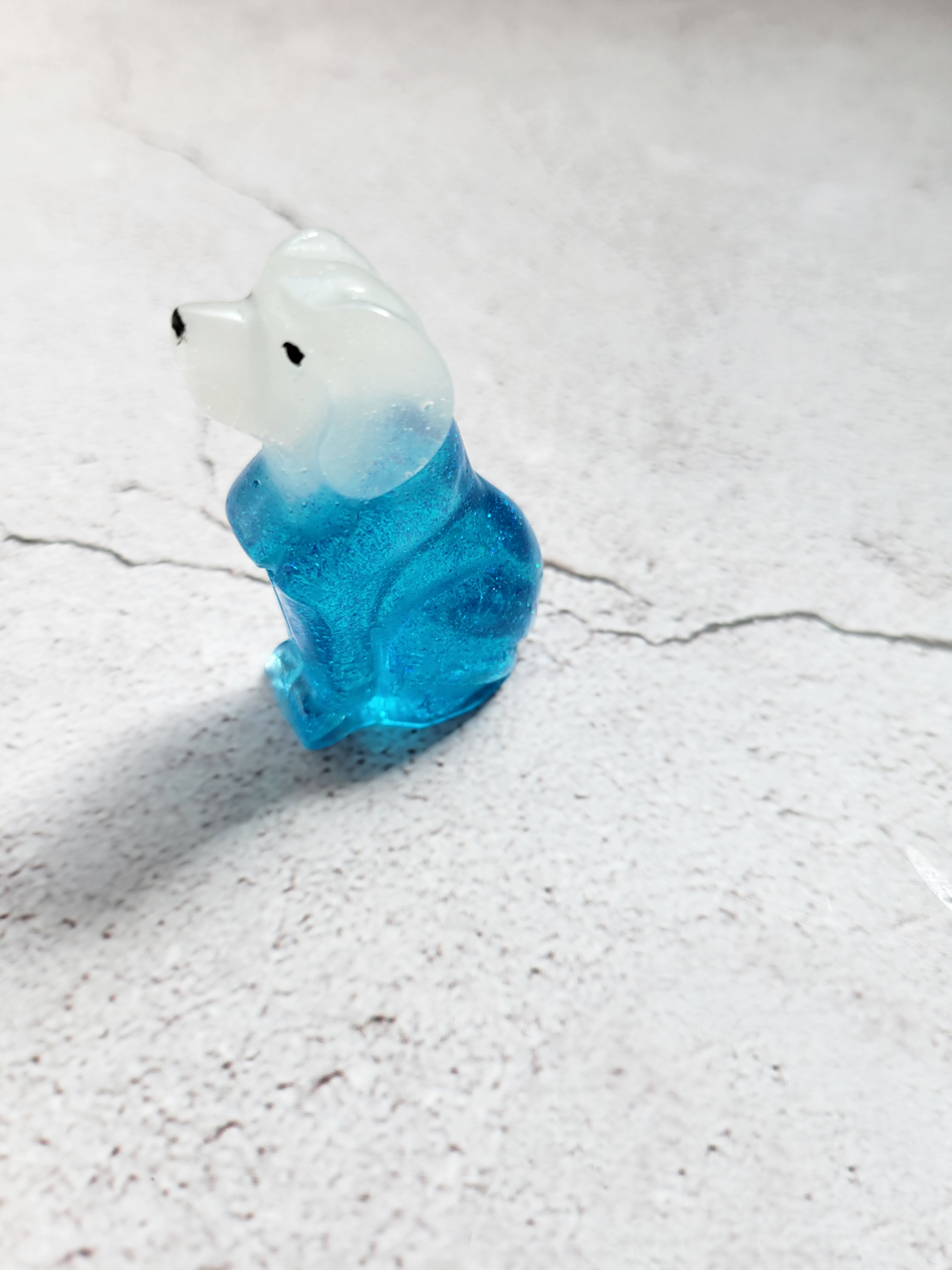 A side view of a tall slim dog figure with a translucent blue body, white head, black painted eyes and nose.