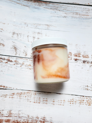 A side view of a 12oz marbled candle to show the brown swirls in the wax. It's in a glass jar with a white lid. This candle is called Casual: Peanut Butter Cookie. It's scent profile is sugar, peanut butter.