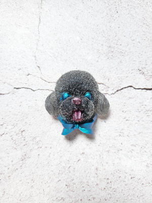 A black dog magnet with red nose and tongue, blue eyes and blue ribbon under its chin.
