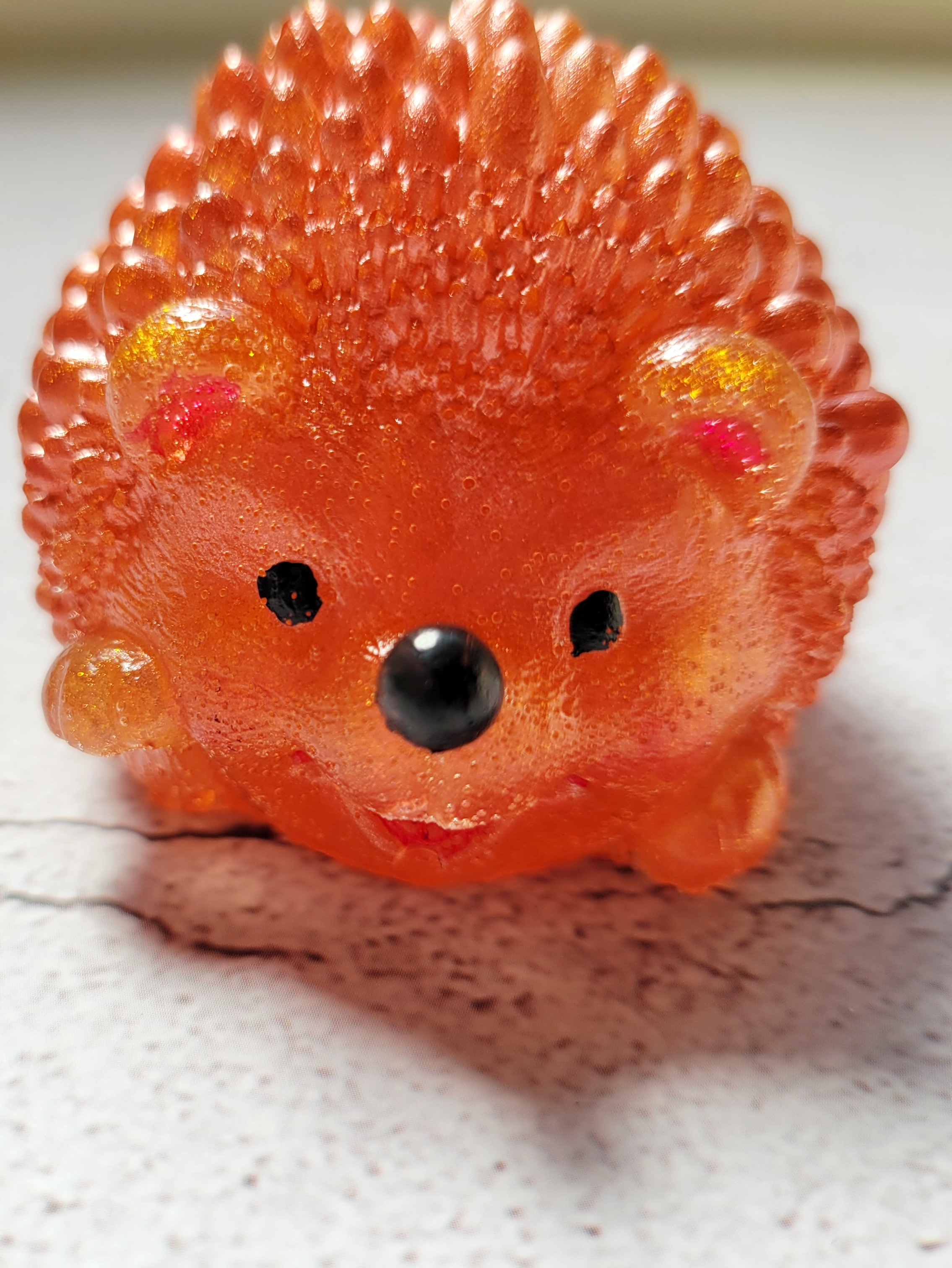 A front view of a hedgehog figure. It has black painted eyes and nose. It's ears and mouth are painted red. It's a dark orange color. It's front paw is raised slightly.