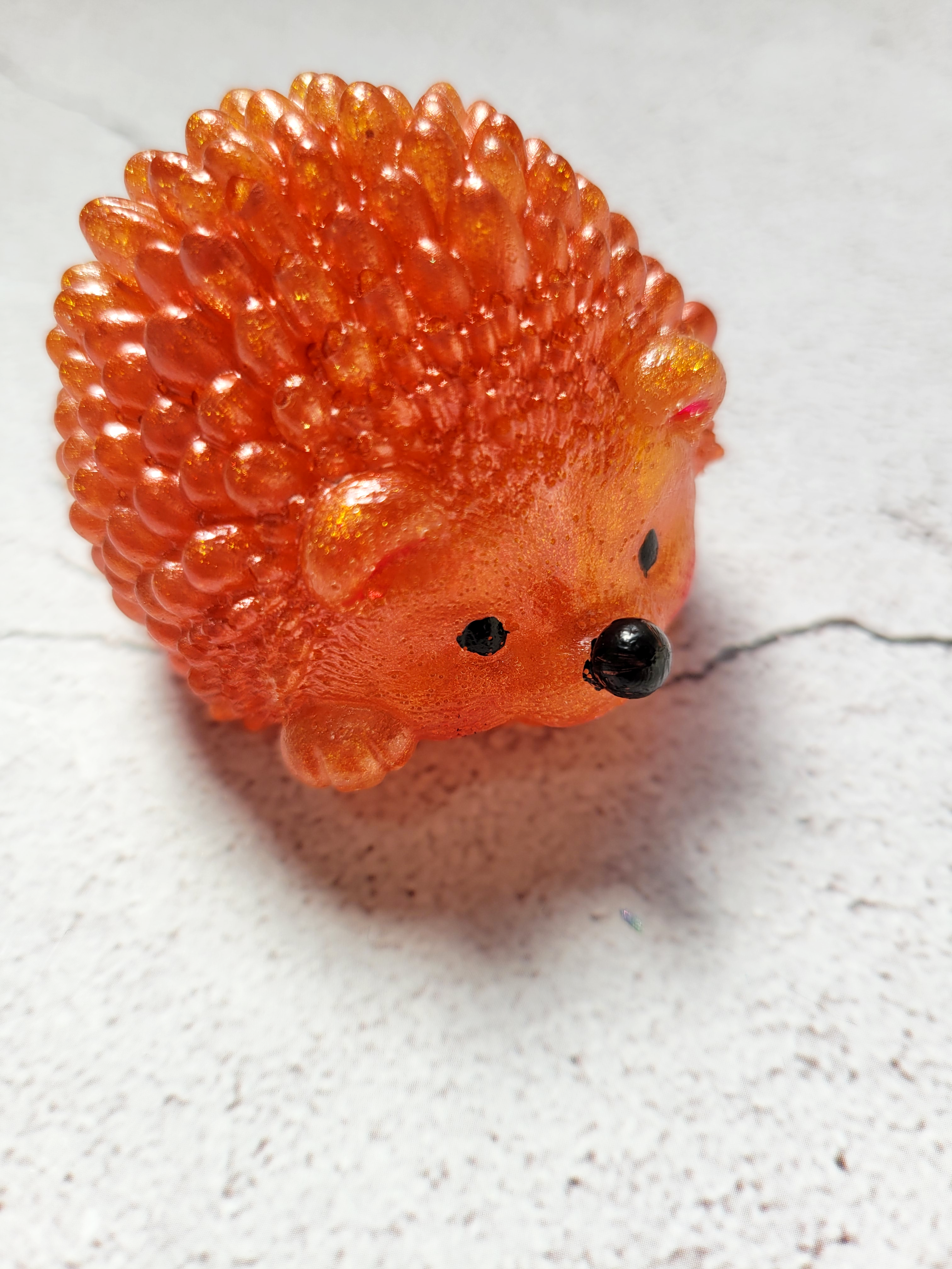 A Top view of a hedgehog figure. It has black painted eyes and nose. It's ears and mouth are painted red. It's a dark orange color. It's front paw is raised slightly.