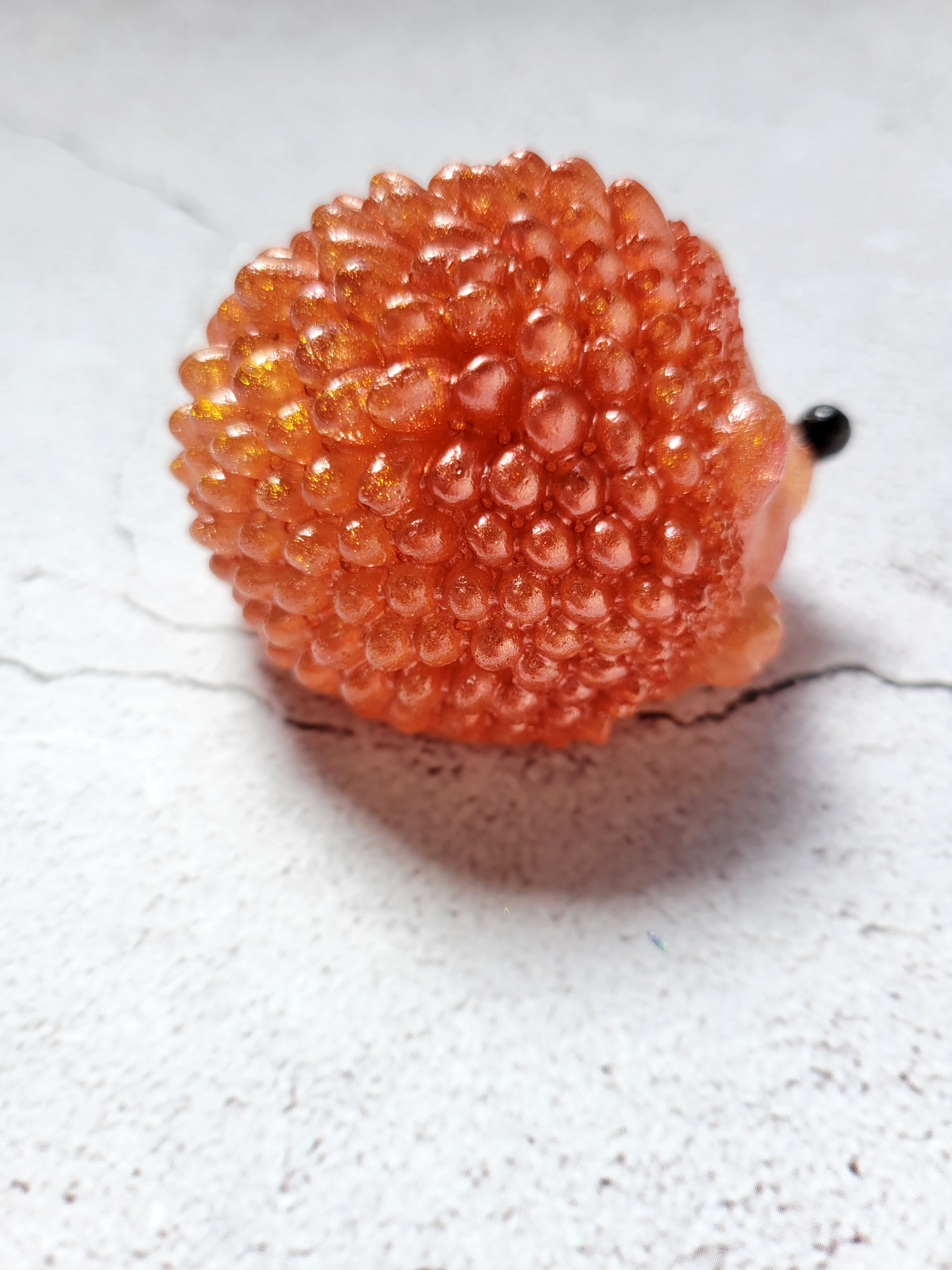A side view of a hedgehog figure. It has black painted eyes and nose. It's ears and mouth are painted red. It's a dark orange color. It's front paw is raised slightly.