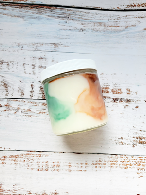 A 12oz marbled candle on its side to show the green and brown swirls in the wax. It's in a glass jar with a white lid.