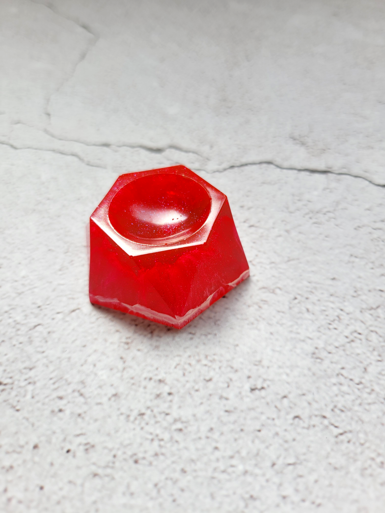 A hexagonal stand for dice or a Tabletop Familiar. It's red with white plumes of ink inside. This is a side view.