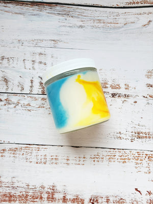 A 12oz marbled candle on its side to show the blue and yellow swirls in the white wax. It's in a glass jar with a white lid. The scent is called Casual Candle: Marshmallow Peeps