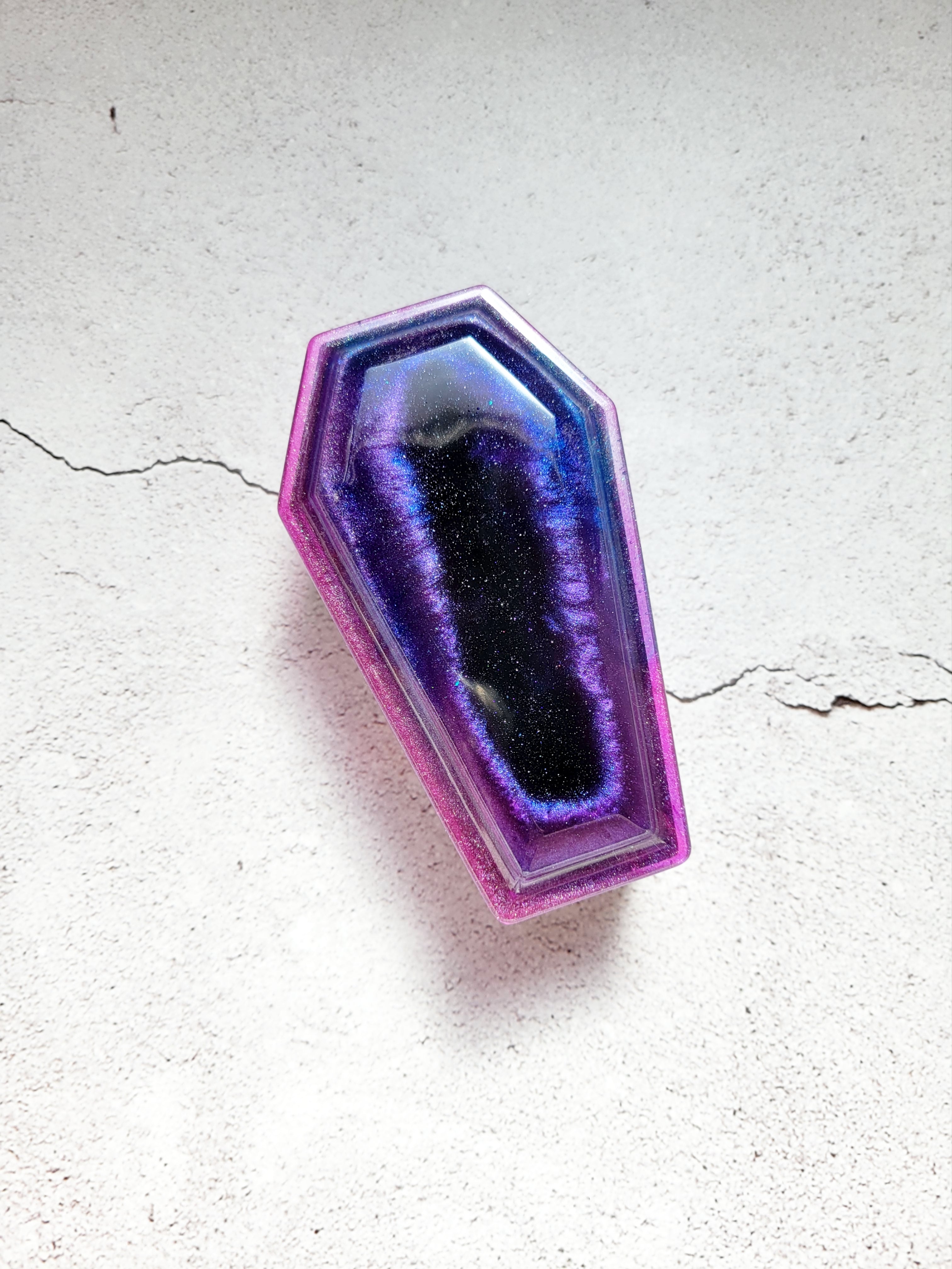 a resin made dice coffin, closed lid, in shimmering blues, purples, pinks, and black