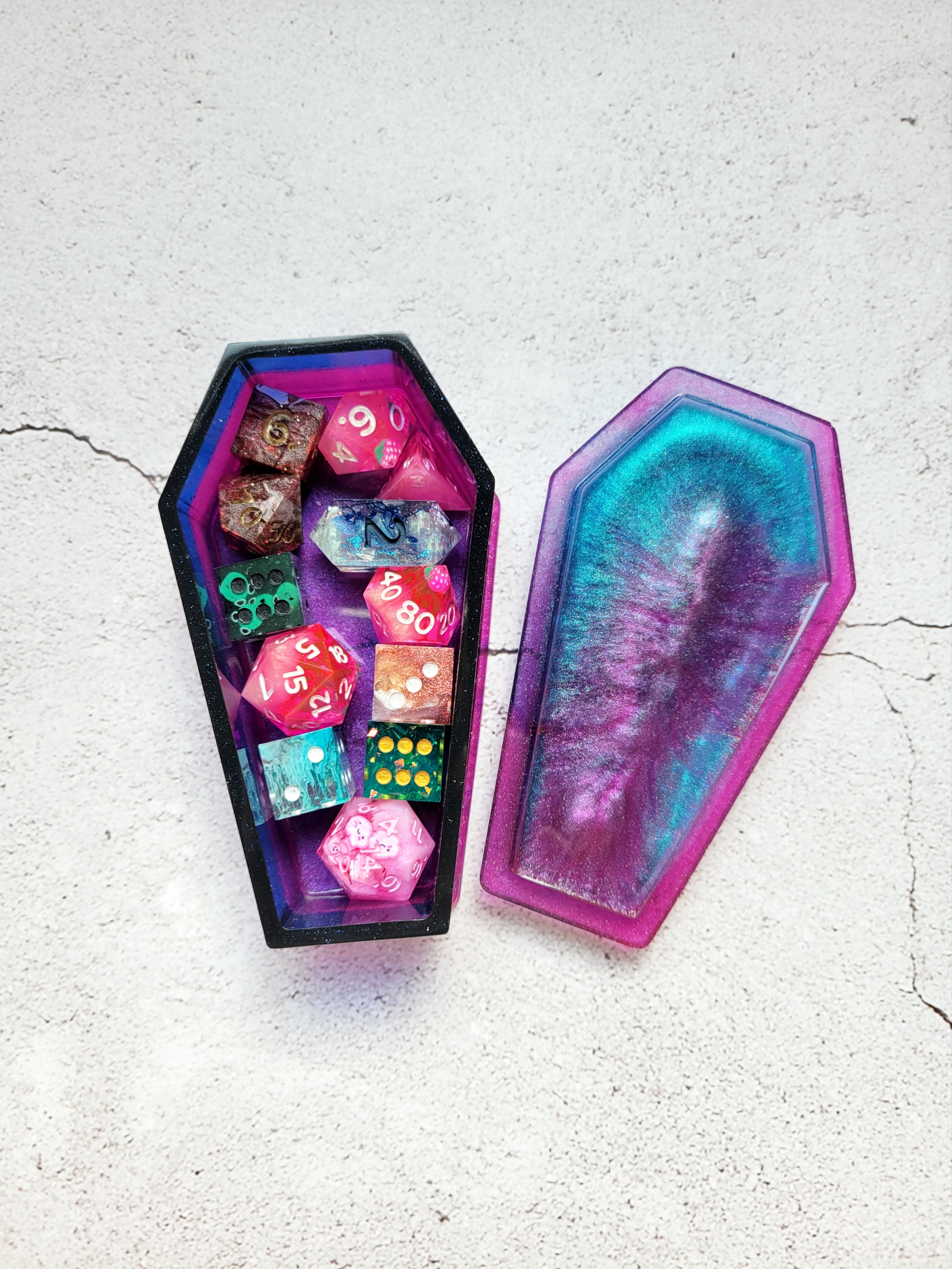 a resin made dice coffin, open lid to show the dice inside, in shimmering blues, purples, pinks, and black