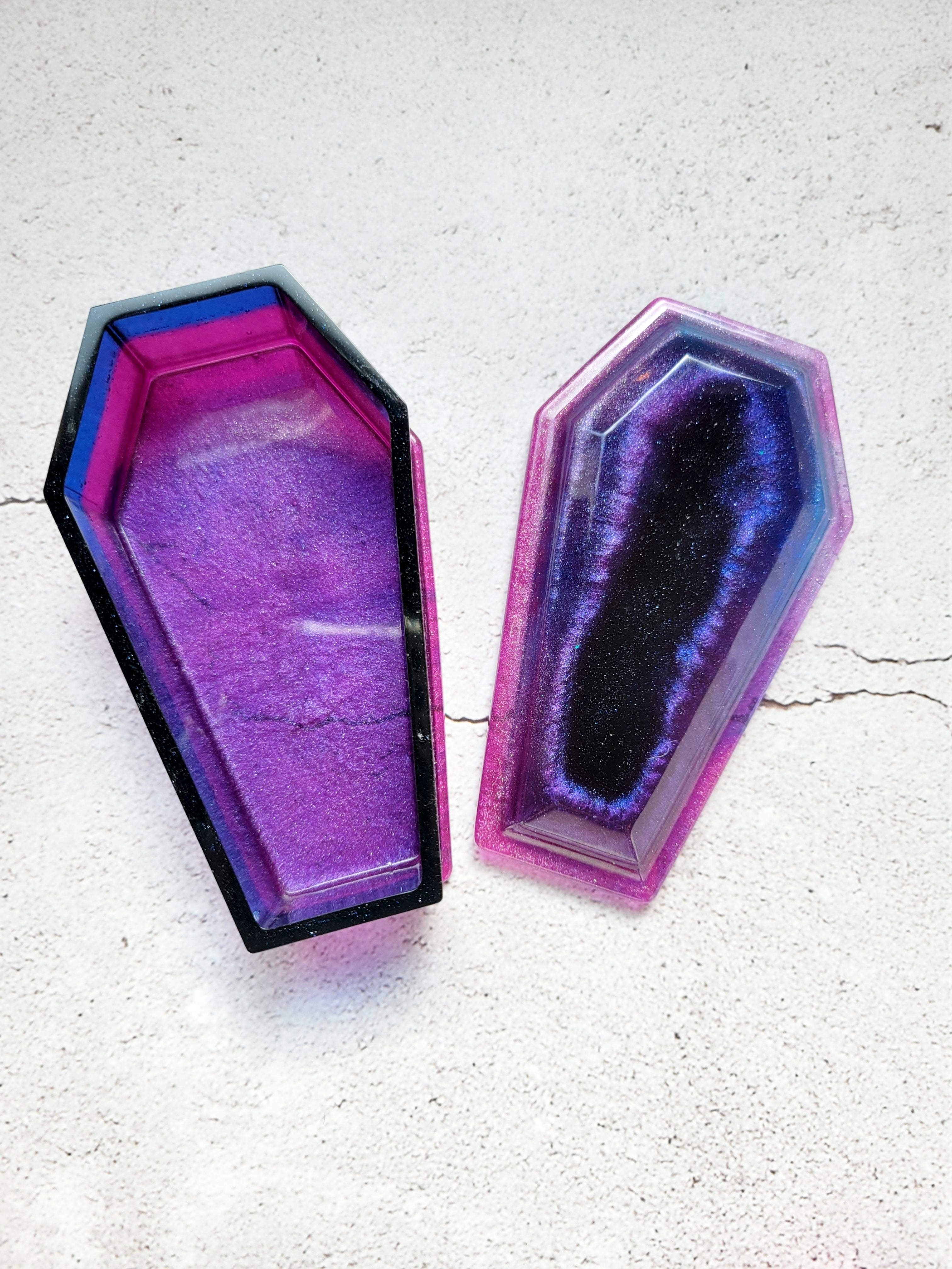 a resin made dice coffin, open lid, in shimmering blues, purples, pinks, and black - no dice in this image