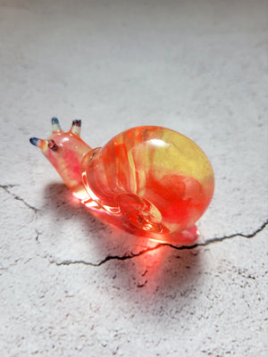 a resin made snail, back view. a clear yellow and orange swirl coloring with blue topped antennae
