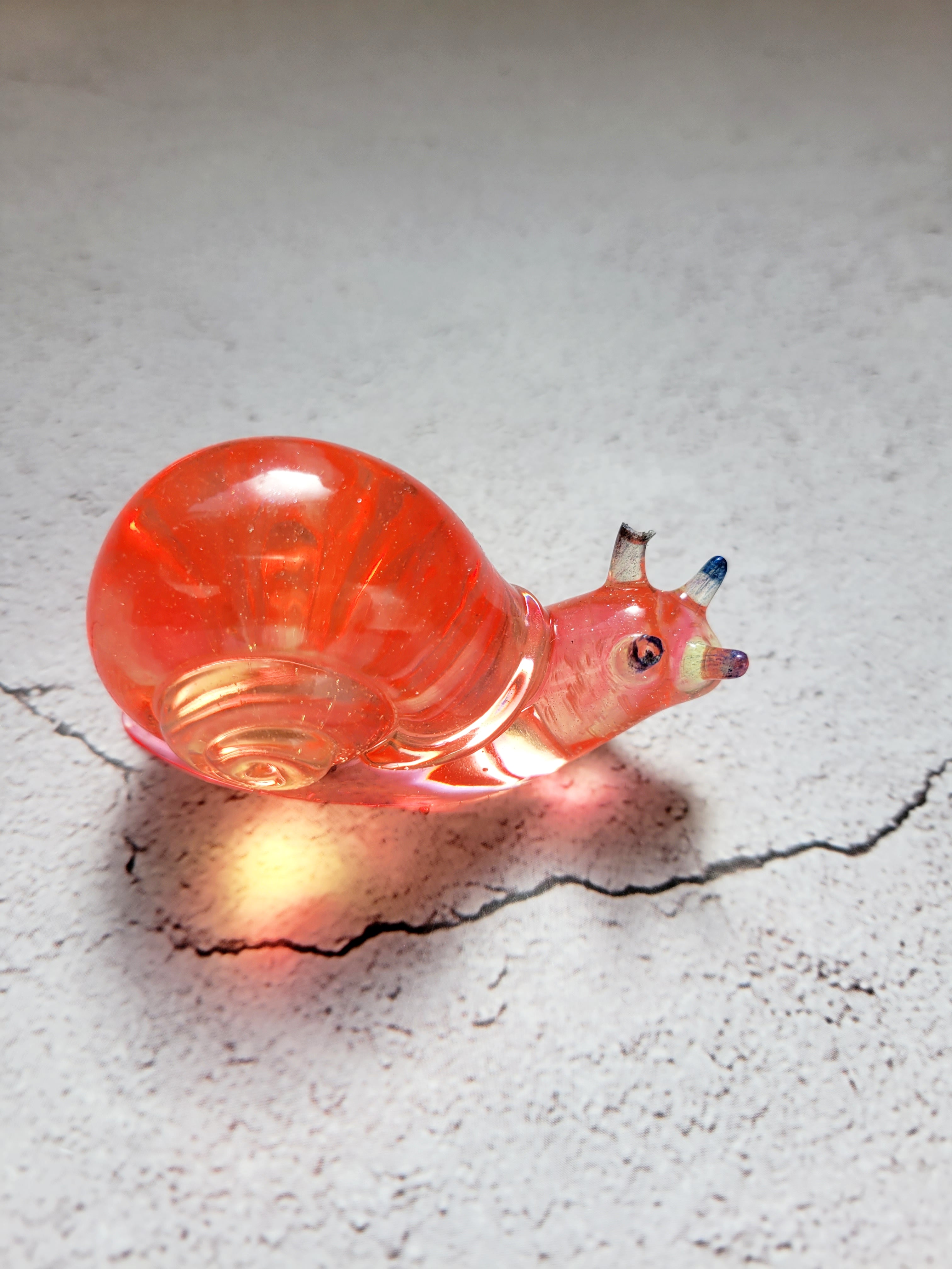 a resin made snail, side view. a clear yellow and orange swirl coloring with blue topped antennae