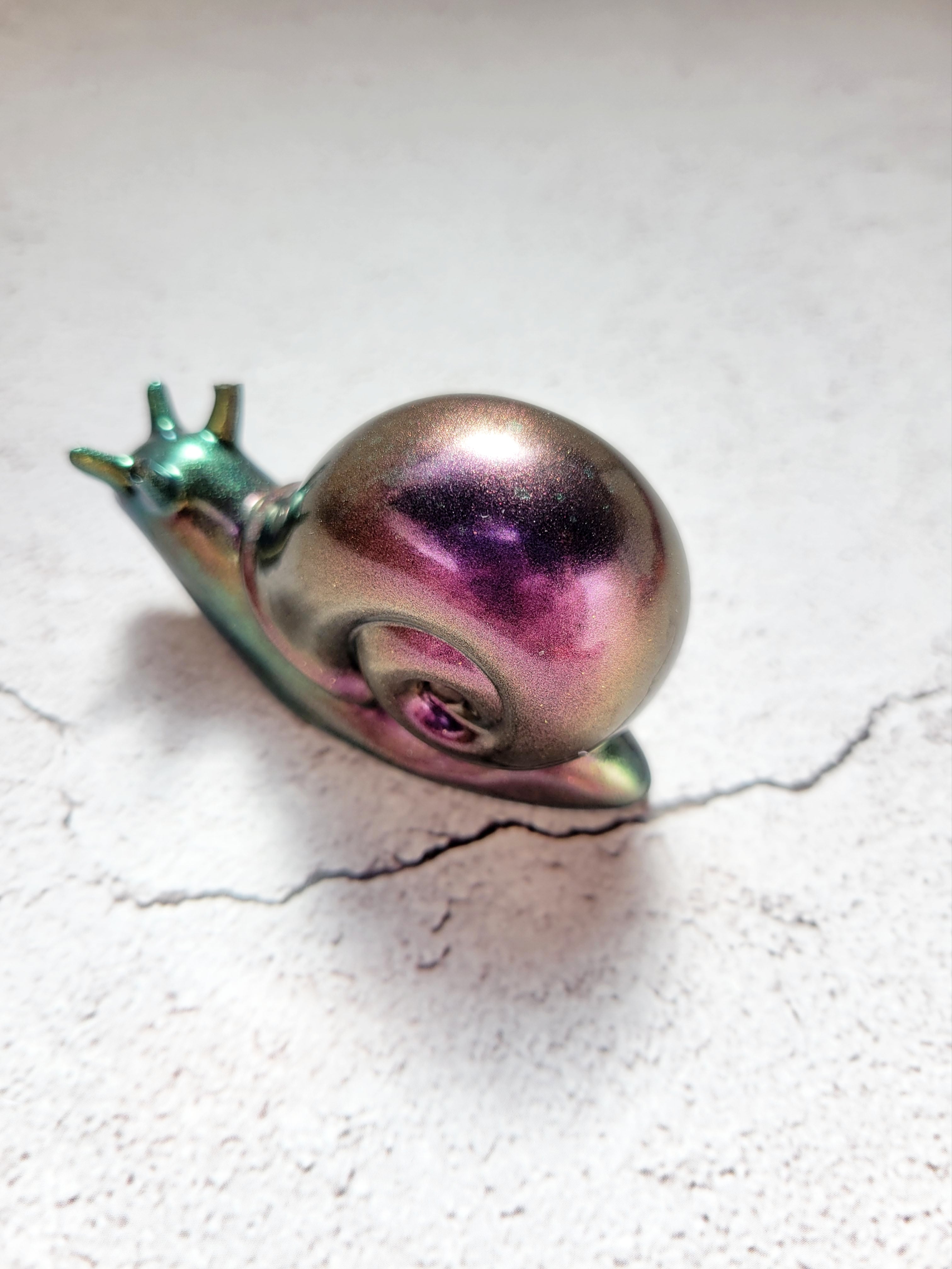 a resin made snail in color shifting colors of shimmering green (body) and purple (shell) back view