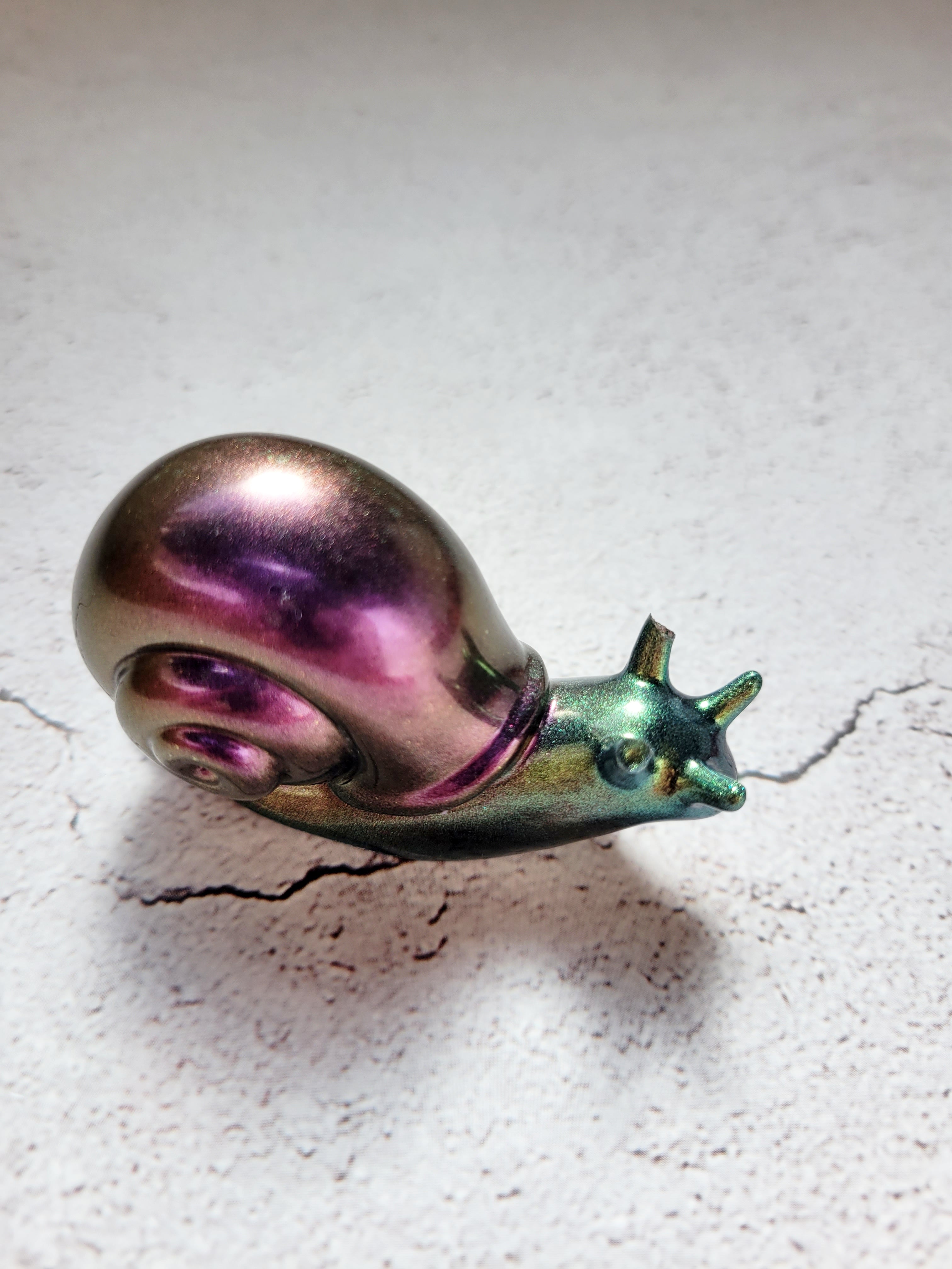 a resin made snail in color shifting colors of shimmering green (body) and purple (shell) front view