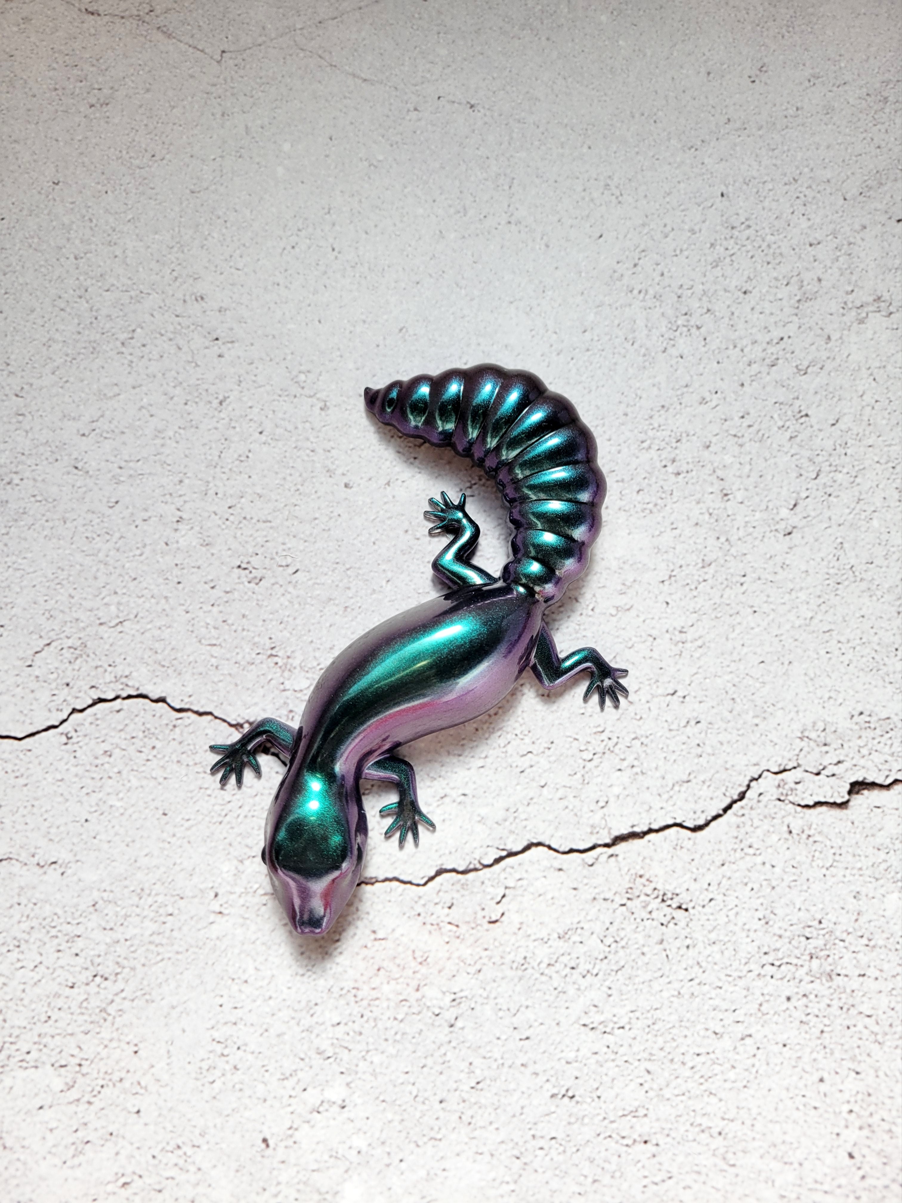 a resin made lizard in color shifting colors of shimmering blues, purples, greens. with black painted eyes. top view