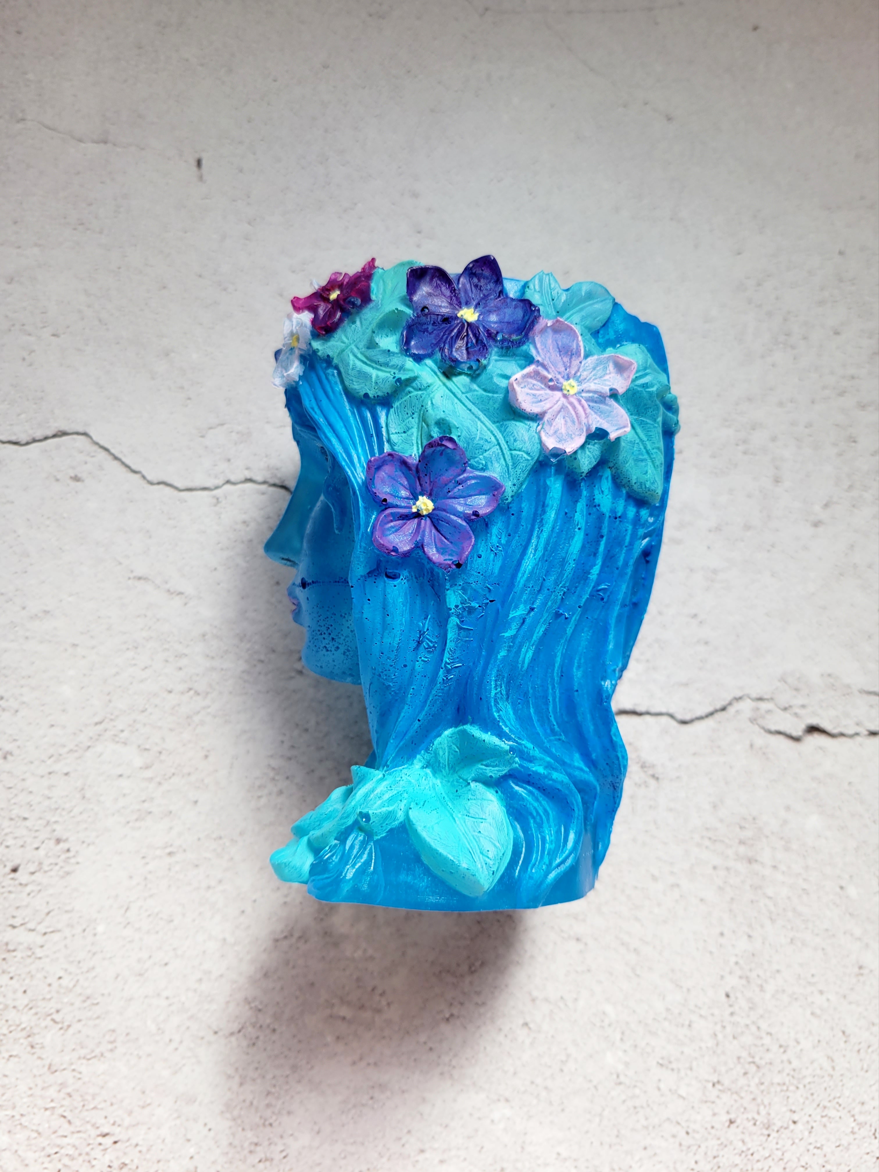 a resin made female ancient statue bust, blue in color with painted leaves and flowers. side view