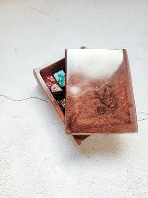 a resin made dice tome box, partially open to show the dice inside. It's a shimmering brown and black color.