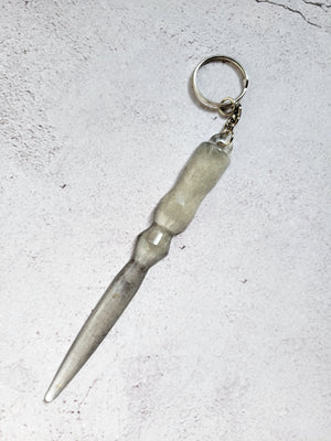 A defense keychain that looks like a wand. There is a silver hoop and chain. it's transparent black and white.